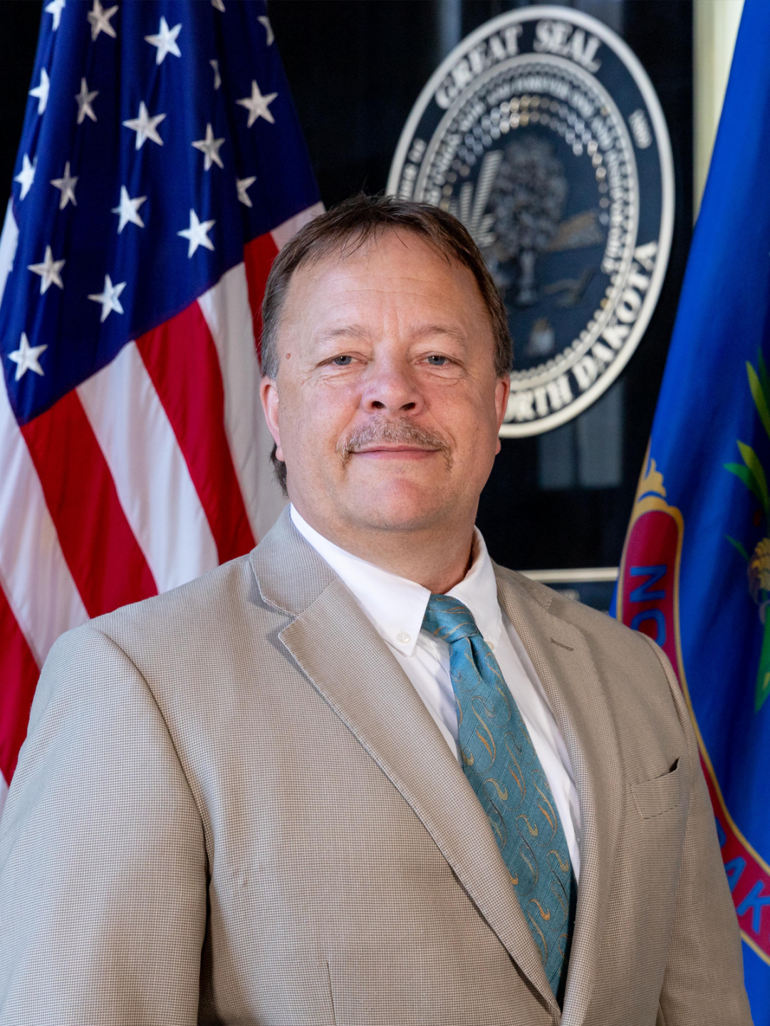 Image of Governor Henke Ron standing in front of the great seal and national flag.