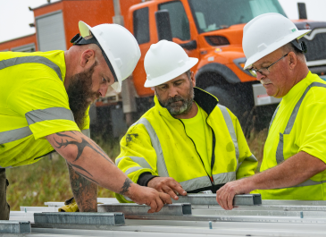 Three construction workers in the field working on a project together.