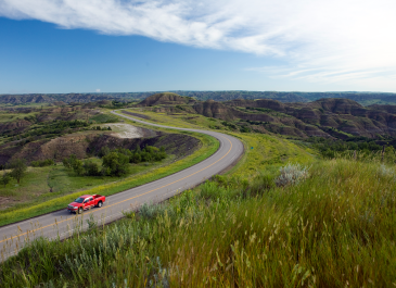 Red pickup drives on road near Theodore Roosevelt National Park in North Dakota.