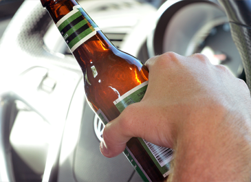 Hand holding a bottle of beer while driving.