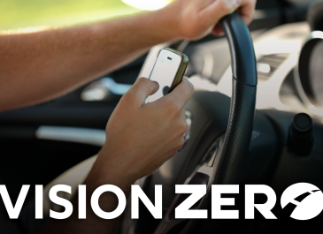 Hands holding a cell phone and texting while driving with a Vision Zero logo at the bottom.