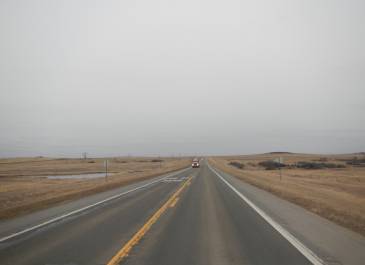 A portion of the US 85 two lane highway with oncoming traffic. Sky is gray with dry grass. 