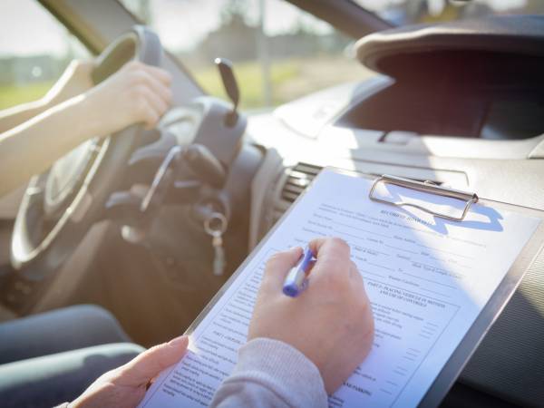 Person driving a car while an instructor takes notes