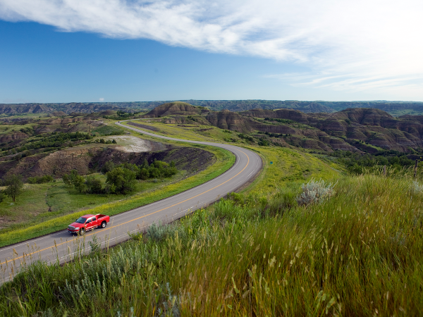 Red pickup drives on road near Theodore Roosevelt National Park in North Dakota.