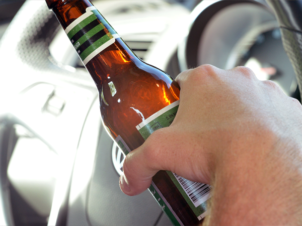 Hand holding a bottle of beer while driving.