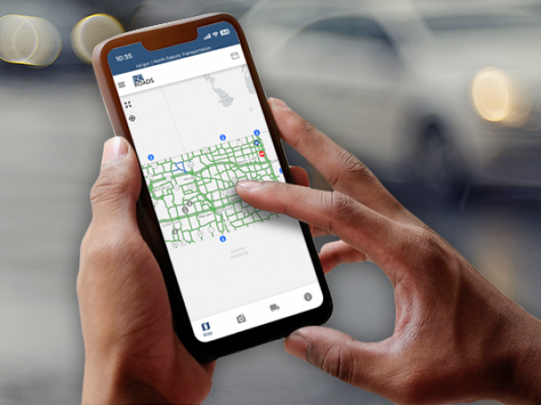 Hands holding a mobile device using the ND Roads app.
