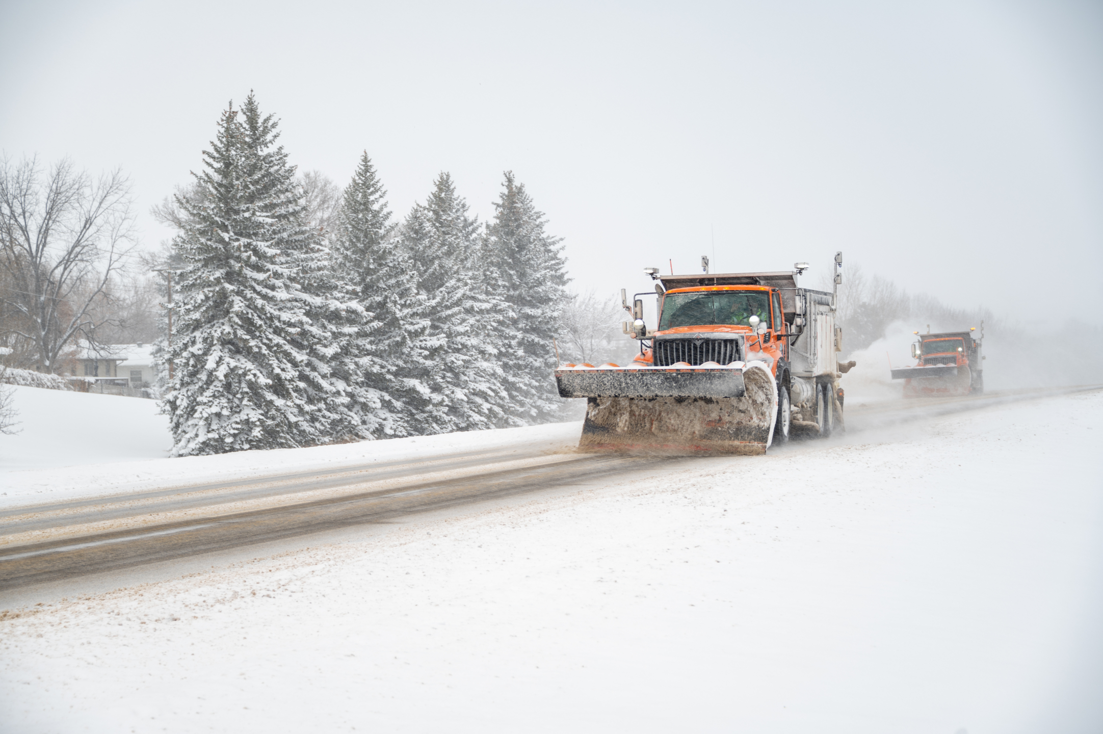 A snowplow clears the highway as another snowplow follows in the distance.