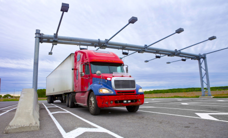 Large red logistics truck passing through weight scanners on interstate.