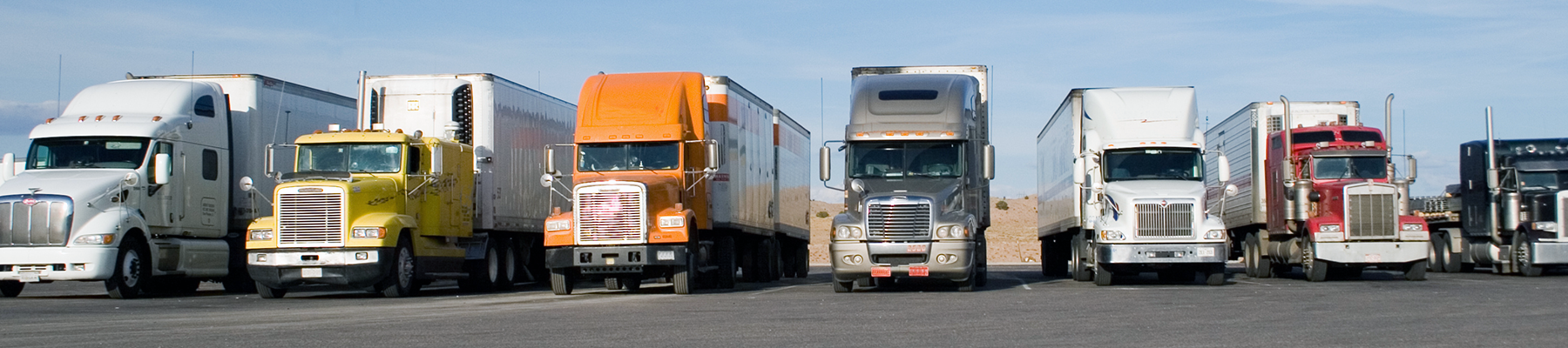 Row of semi trucks parked in a truck stop parking lot.