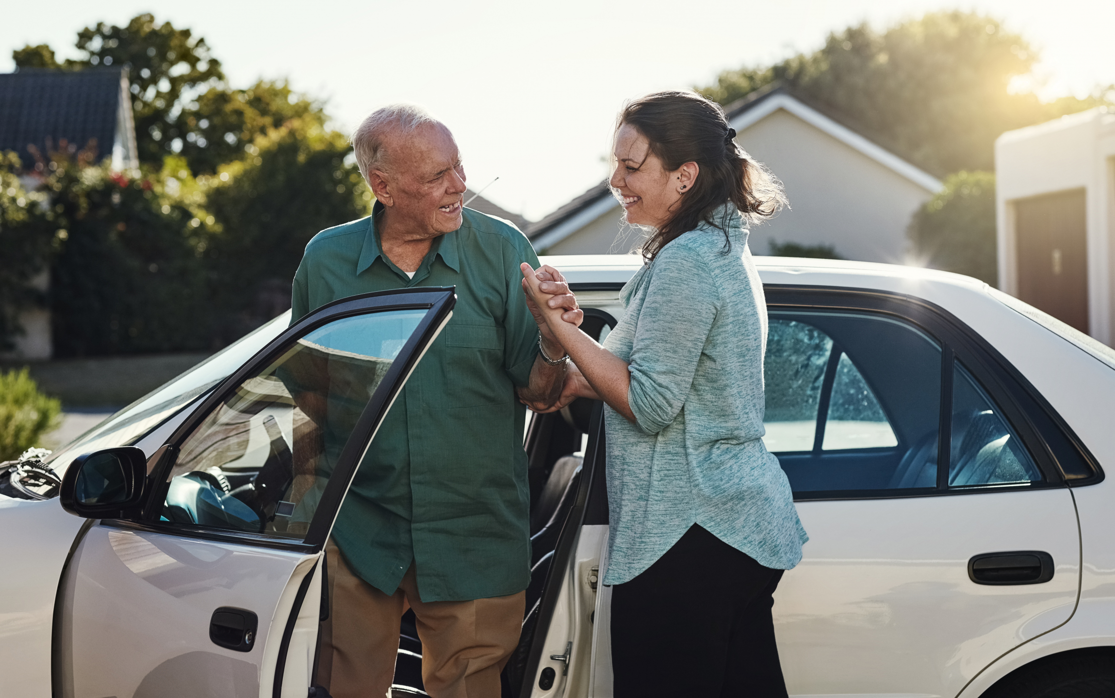 Senior man and caregiver smiling and talking while standing next to a car.