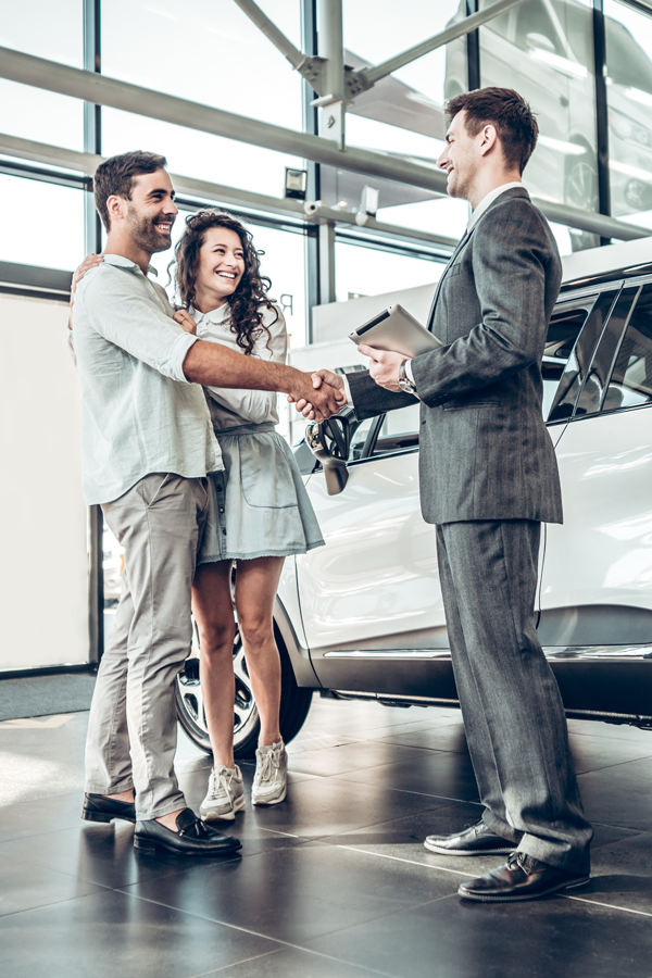 Young couple shake hands with car salesman at a dealership.