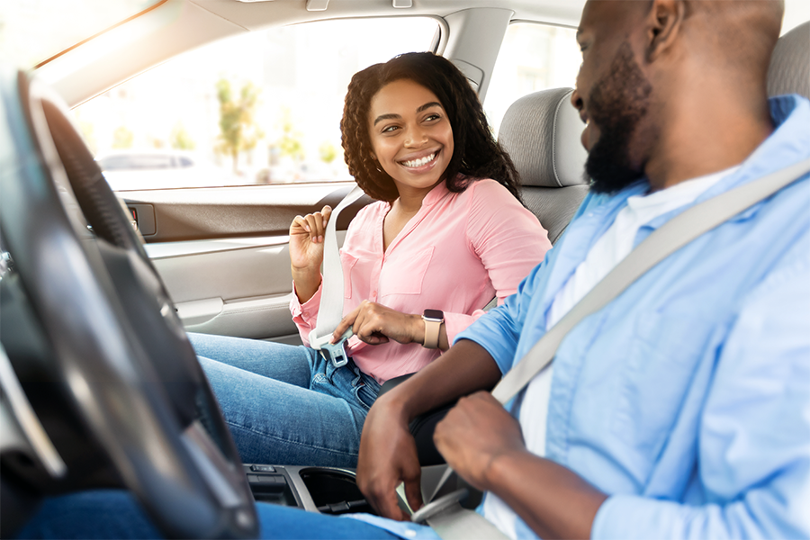 A man and a woman happily fasten their seatbelts before they go for a drive.