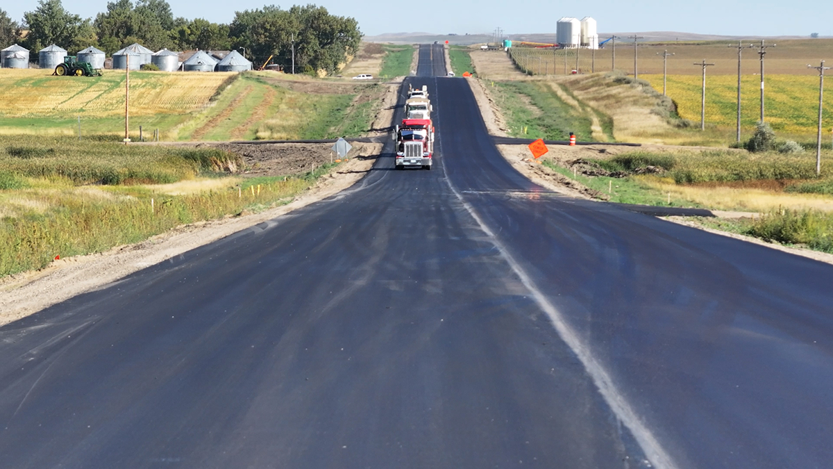 an image of trucks rolling down a freshly paved road,from the award winning project
