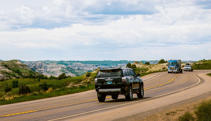 Vehicles driving along road in the midst of mountain ranges.