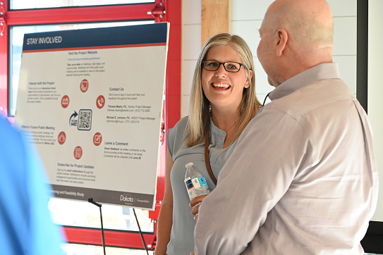 Woman and man standing next to an open house display board talking.