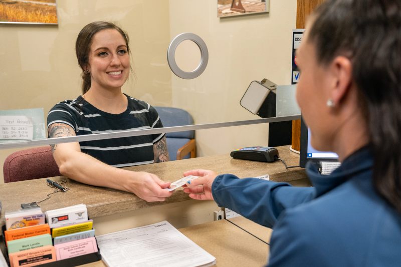 Young woman receives her new North Dakota driver license from smiling NDDOT employee.