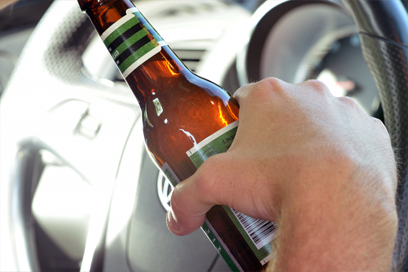 Hand holding a bottle of beer while driving.