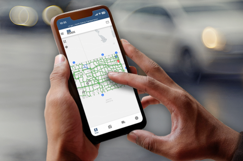 Hands holding a mobile device using the ND Roads app.