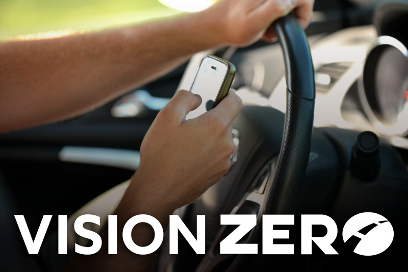 Hands holding a cell phone and texting while driving with a Vision Zero logo at the bottom.